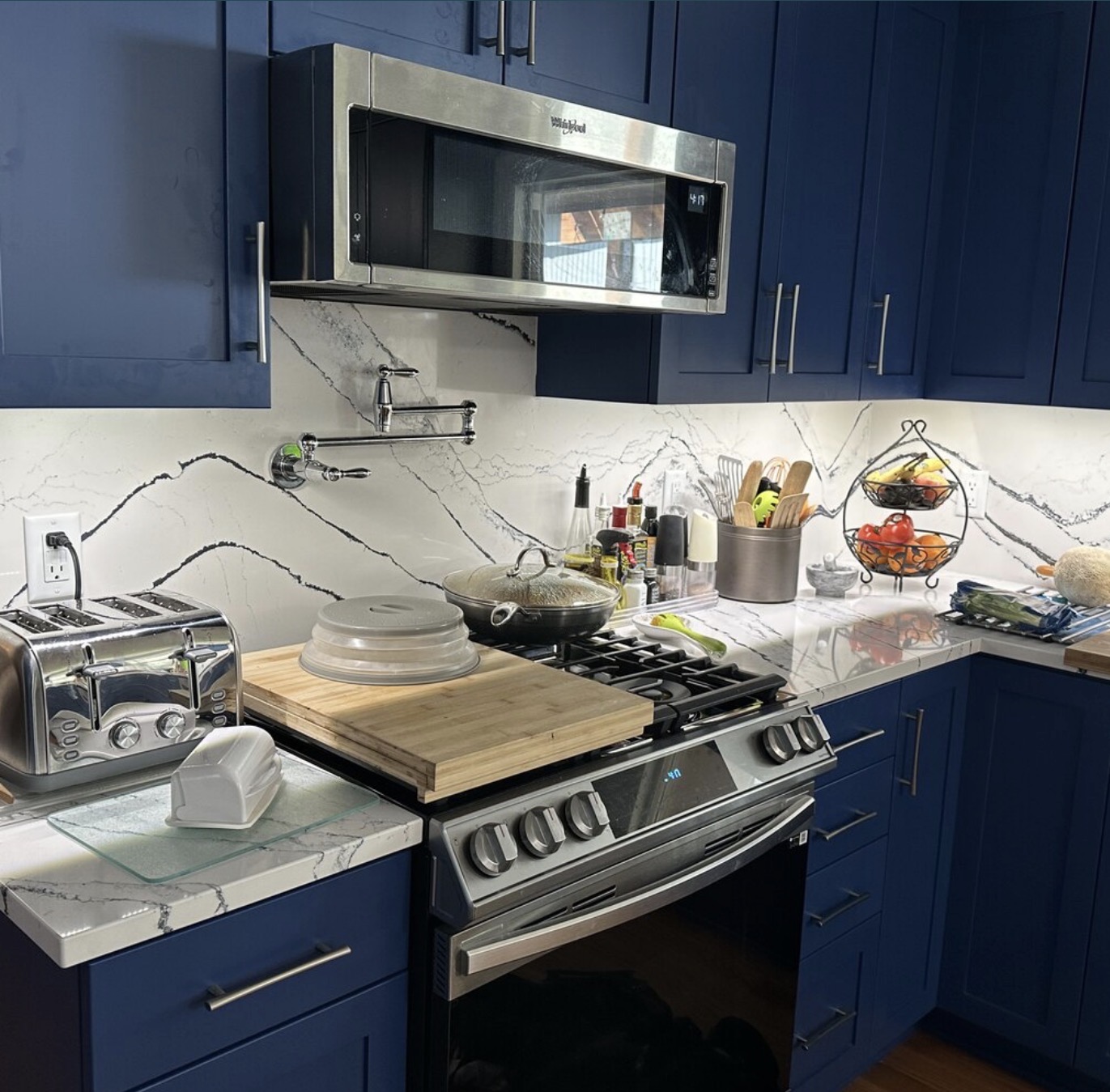 Kitchen remodel with navy blue cabinetry, quartz backsplash, and stainless steel appliances by Righteous Renovations